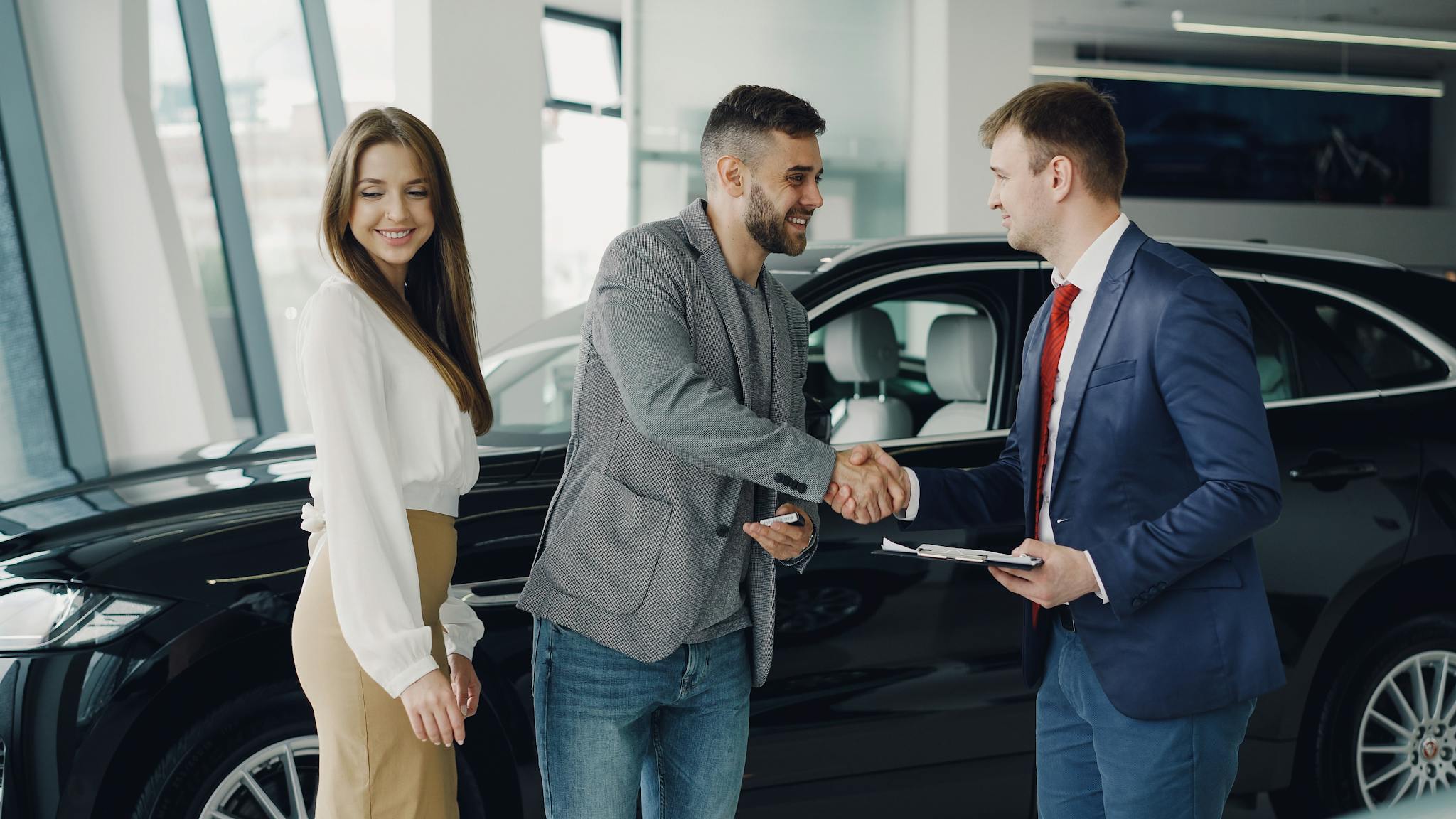 Buyers and sales representative shake hands at a car dealership for a successful car purchase.