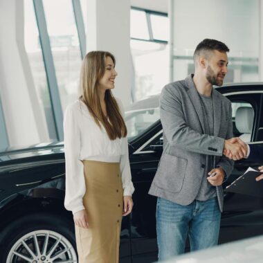 Customers shaking hands with dealer in showroom, sealing car purchase deal.