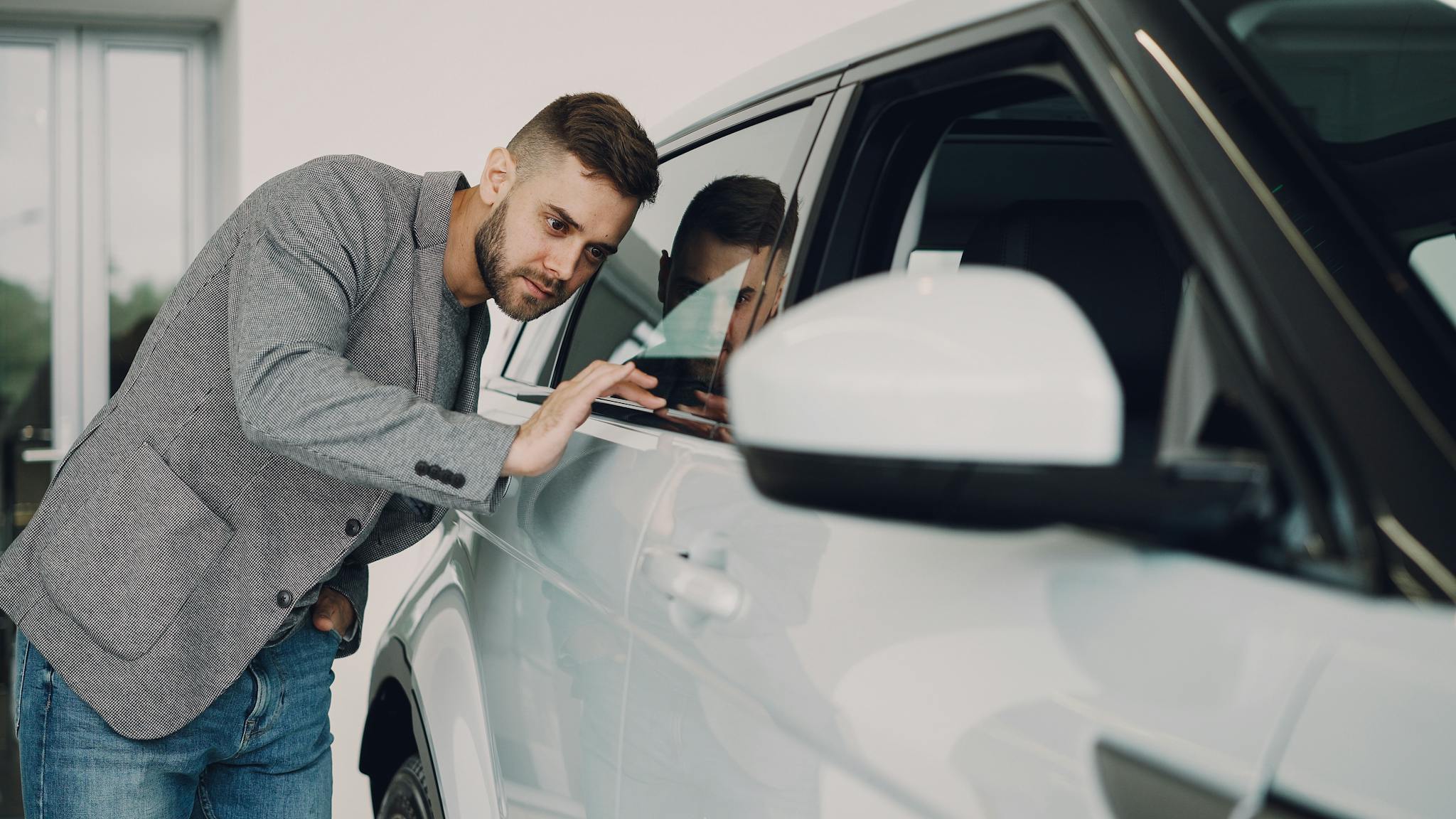 Man carefully examining a modern white car at a dealership showroom.